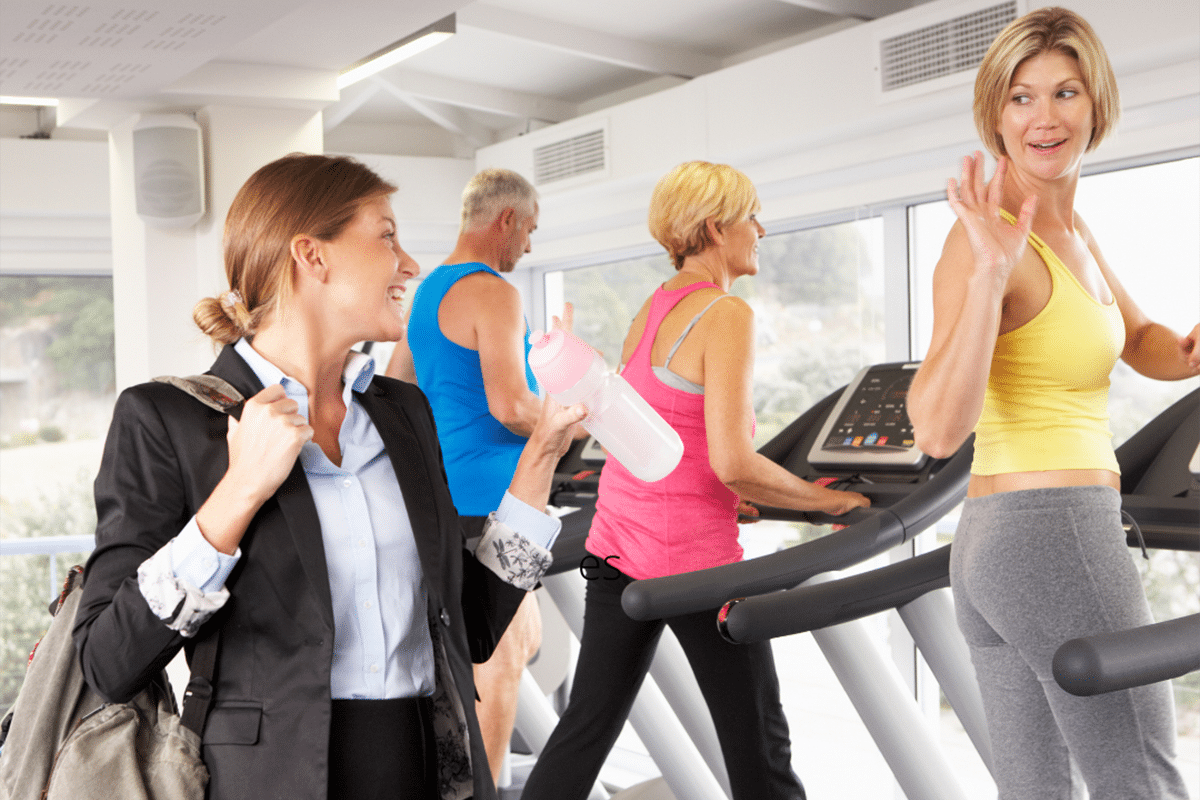 Business woman waving at friends walking on treadmills