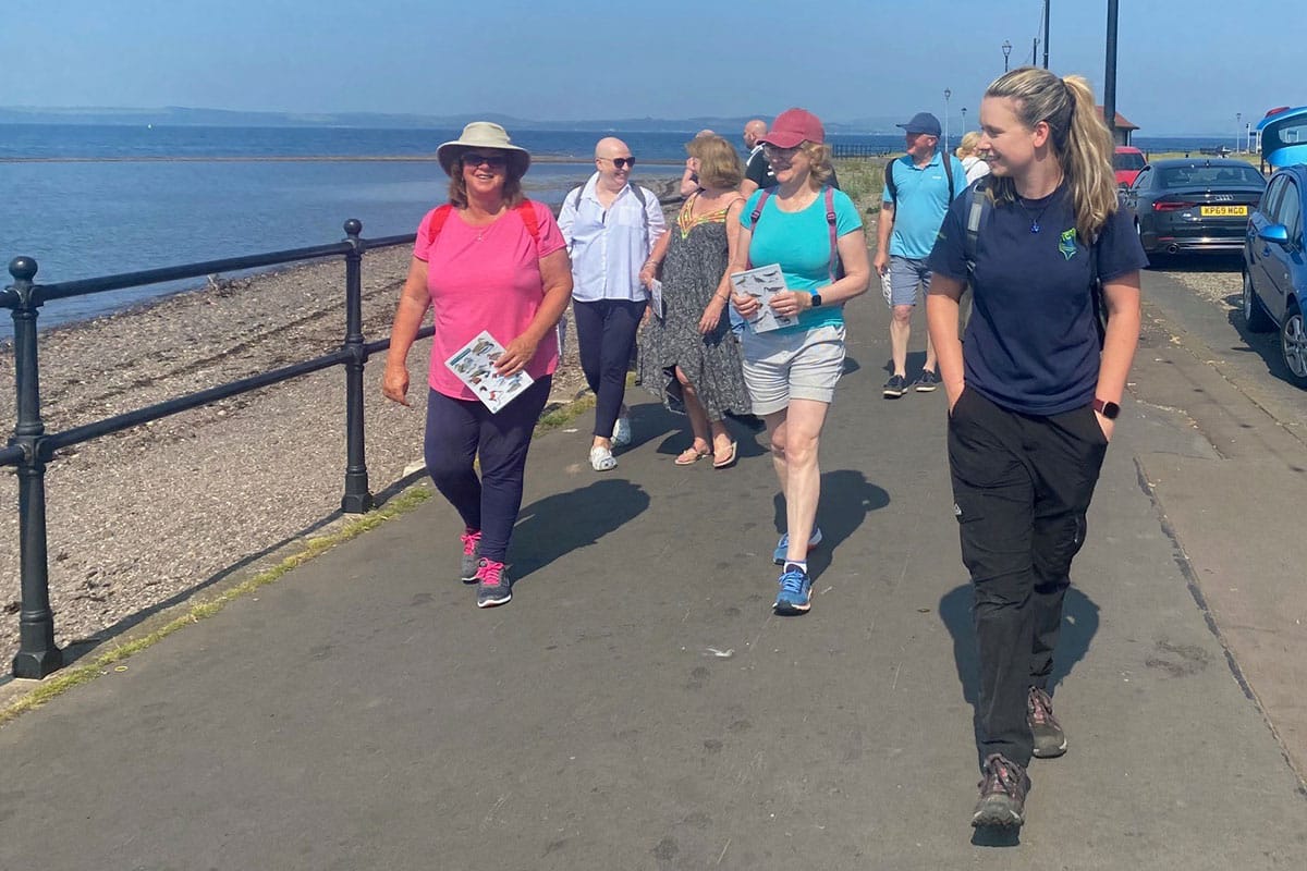 Volunteer leading a group of walkers along seaside path