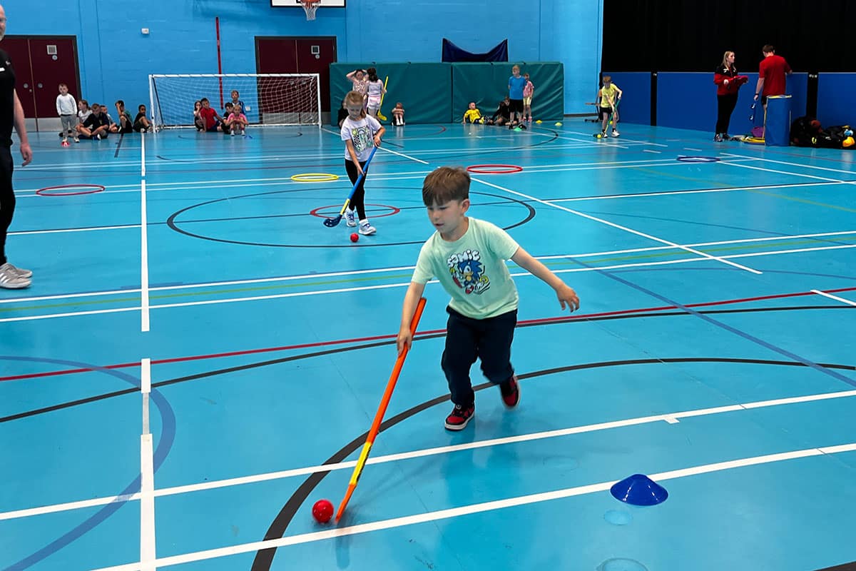Children playing hockey in sports hall