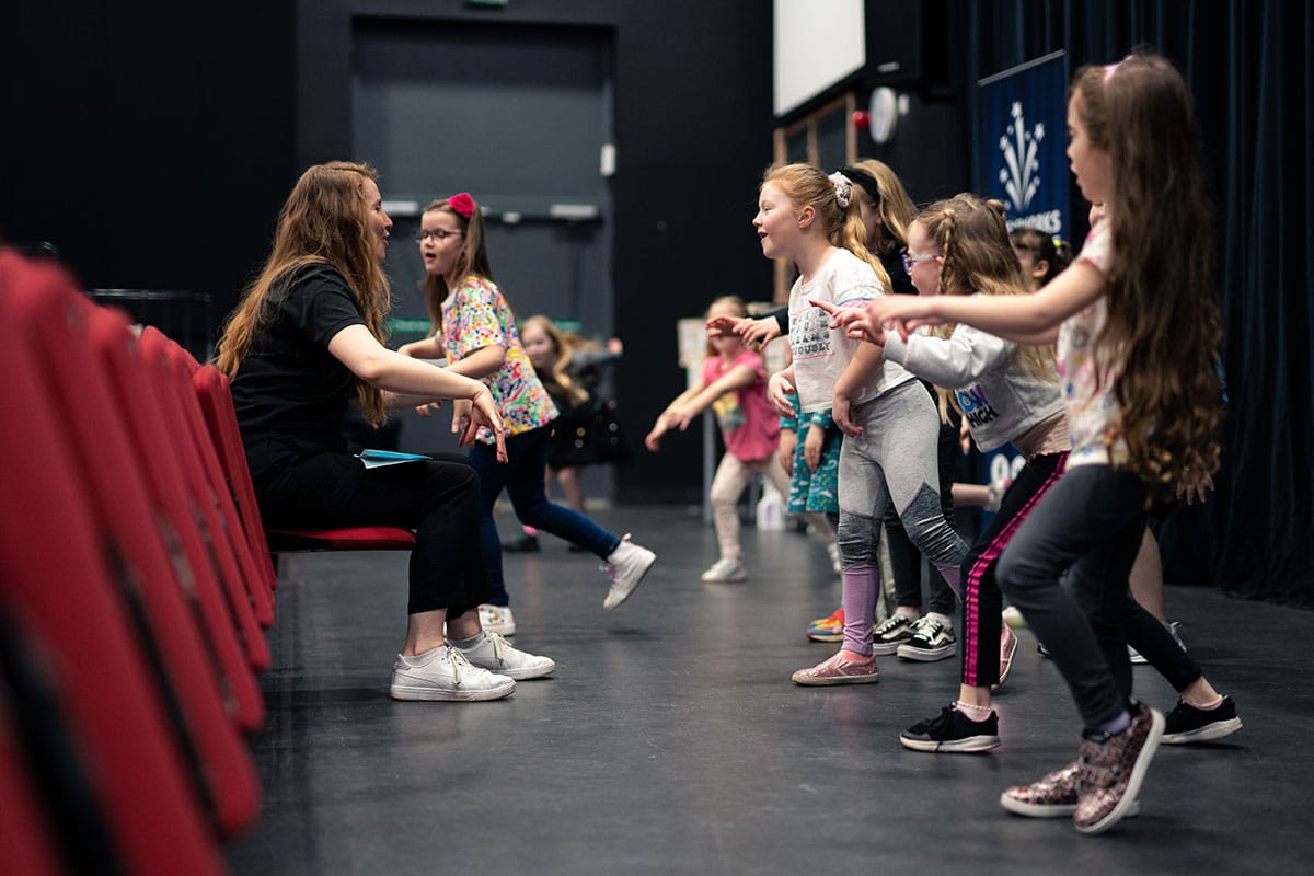 Instructor encouraging children as they explore drama and performance