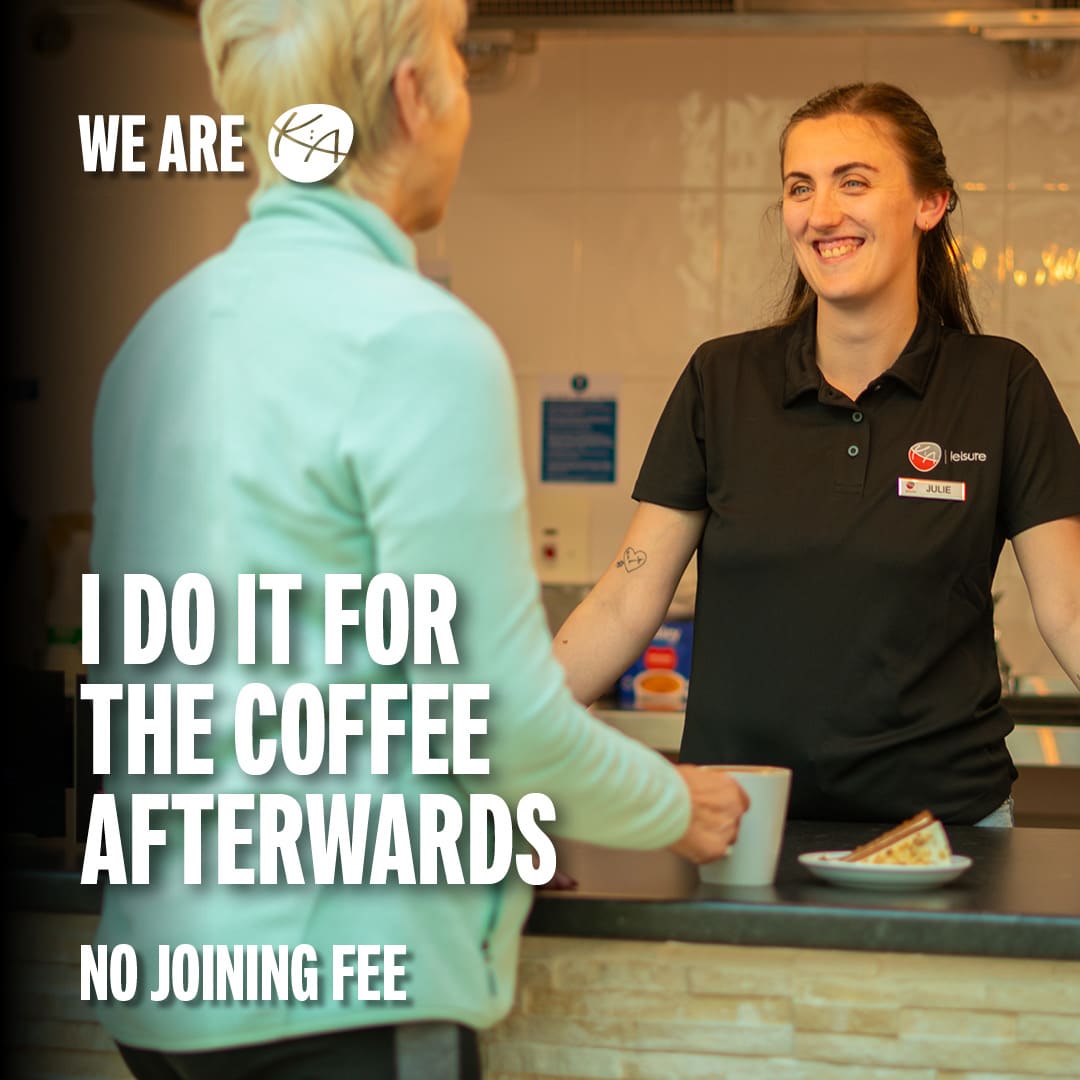 An older female is greeted by a cheerful female member of staff when buying her coffee from the cafe after her workout