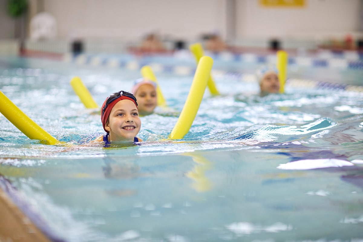 Little girl with swimming noodle Small group of children in pool with swimming aids
